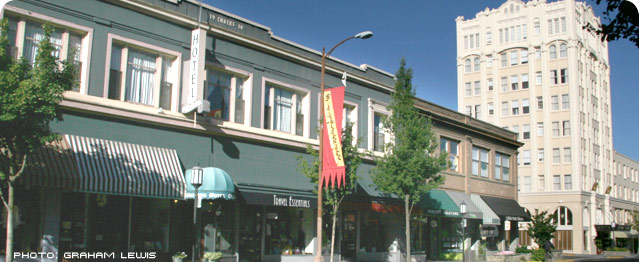 Two story storefront green with cream color trimmed windows on second story, red and yellow flag in front, rectangular tower attached on the right with many windows.