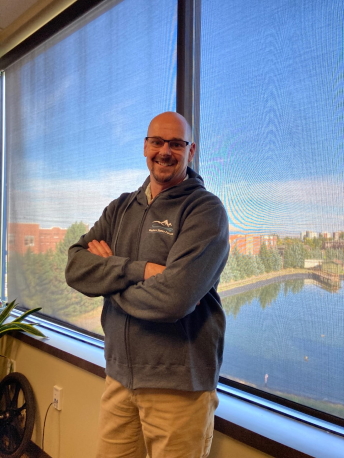 A man with a Forum sweatshirt poses for a photograph in an office.