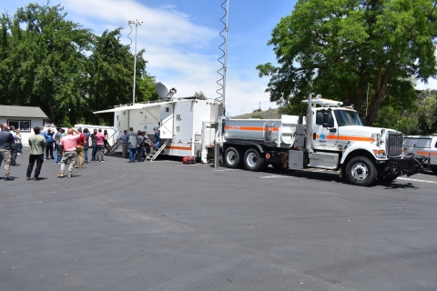 A group of people lines up in front of a large truck and trailer with Caltrans markings and deployed communications antennas.